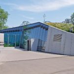 Der dynamisch gestaltete Eingangsbereich mit großzügigen Verglasungen und markanten Sichtbetonflächen. - © Garten-Moser