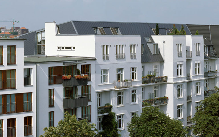 Die Repräsentationsgiebel der 1911 erbauten Gründerzeitgebäude in der Hamburger Isestraße wurden im Krieg zerstört. Die neue Dachaufstockung kommt ganz ohne historisierende Details aus. Glatte, blauschwarze Dachplatten und weiße Putzfassaden verleihen den Gebäuden heute eine moderne Erscheinung.